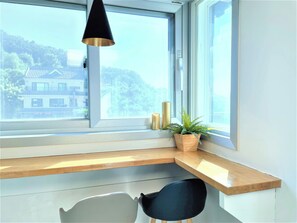 A corner desk with a chair, a potted plant, and a window with a view of buildings and trees. - Incheon airport W Premium guesthouse (Incheon)