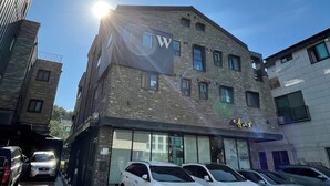 A multi-story building with a prominent 'W' sign on the facade, several windows, and a parking area with cars. - Incheon airport W Premium guesthouse (Incheon)