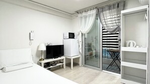A hotel room with a bed, a TV, a microwave, a mini-fridge, a glass door leading to a balcony, and a white wardrobe. - Incheon airport W Premium guesthouse (Incheon)