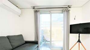 A modern living room with a grey sofa, a glass table, and a TV on a tripod. - Incheon airport W Premium guesthouse (Incheon)