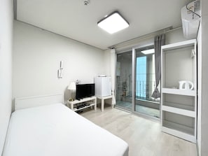 A hotel room with a bed, a TV, a desk with a lamp, a wardrobe, and a sliding glass door leading to a balcony. - Incheon airport W Premium guesthouse (Incheon)