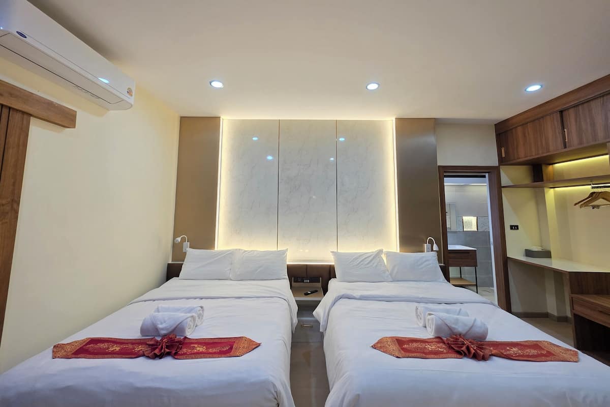 A hotel room with two beds, a minibar, a mirror, and a wooden wardrobe.