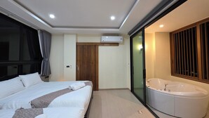 Quarto de hotel moderno com uma cama grande, banheiro separado com banheira e porta de vidro deslizante para uma varanda.
