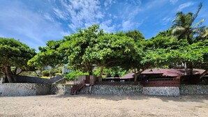 Uma área de praia arenosa com um muro de pedra, uma escadaria e um edifício com telhado vermelho.