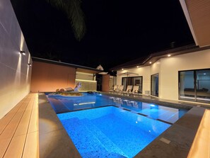 Una piscina con un flotador de unicornio, sillas de descanso y una casa moderna con ventanales grandes.