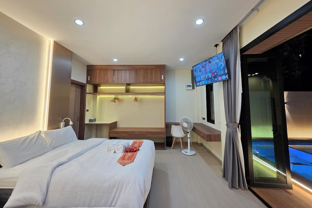 A modern hotel room with a bed, a desk, a TV, and a view of a pool.