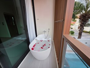 Un baño moderno con una bañera independiente, ducha y puerta de cristal que da a un balcón con vistas a una zona residencial.
