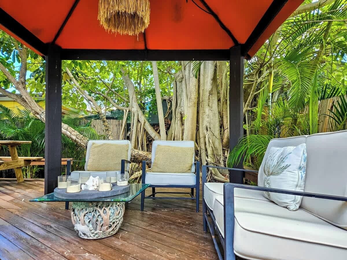 Un área de estar al aire libre con cubierta de madera, dos sillones con cojines, una mesa de vidrio y un sofá.
