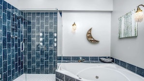 A modern bathroom with a glass-enclosed shower, a freestanding bathtub, and decorative wall art including a crescent moon and a birch tree painting.