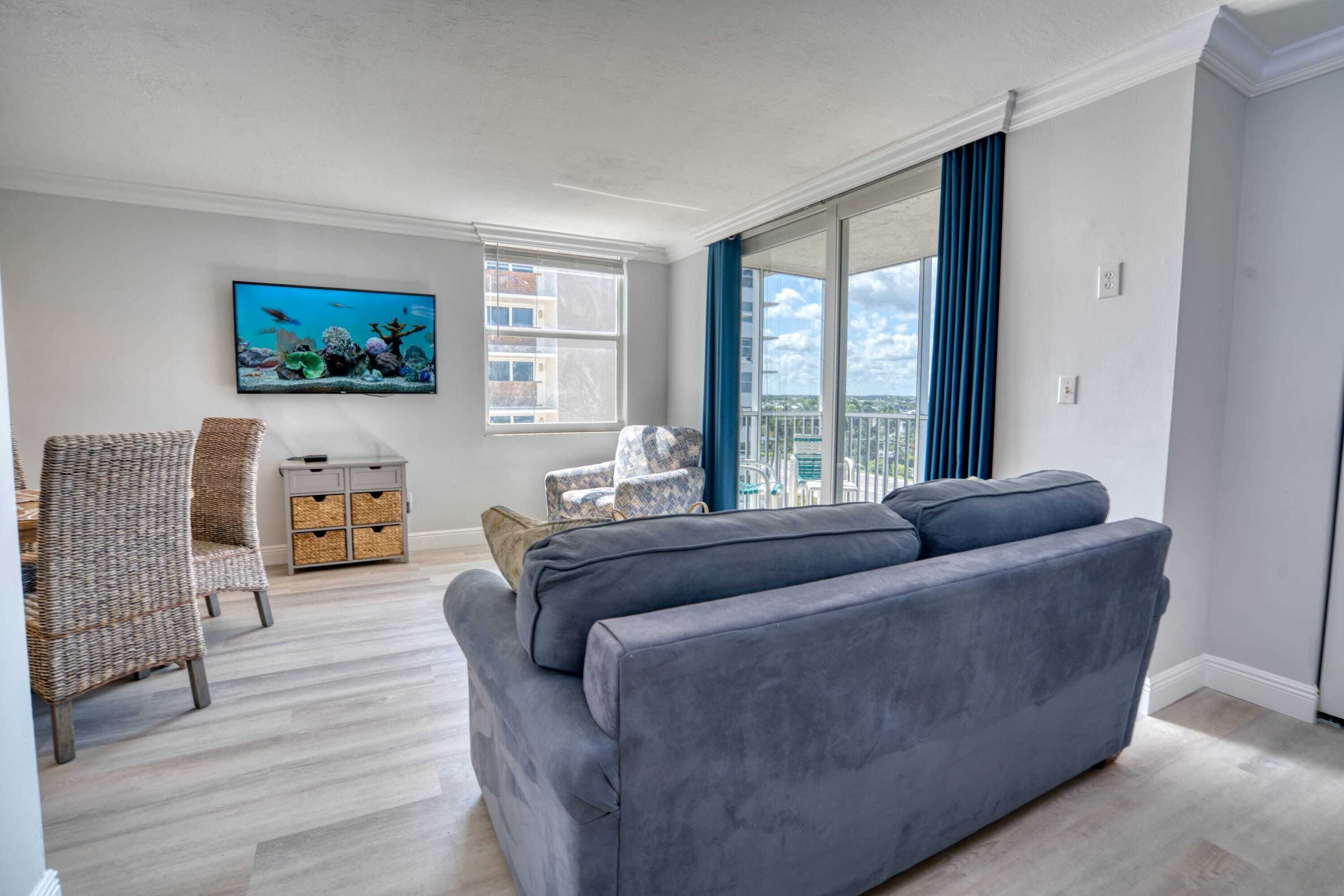 Ein Wohnzimmer mit grauem Sofa, Korbstühlen, Fernseher und Blick auf die Stadt.