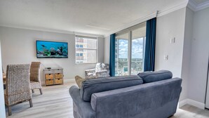 A living room with a grey sofa, wicker chairs, a TV, and a view of the city.