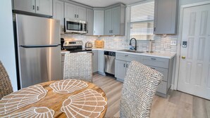 A modern kitchen with white cabinets, stainless steel appliances, and a round wooden table with a shell pattern.