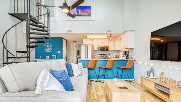 A modern apartment with a spiral staircase, a kitchen with bar stools, a wooden coffee table, and a TV mounted on the wall.