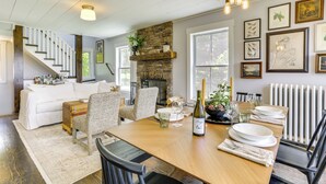 Un coin repas avec une table en bois, des chaises et une cheminée. Un escalier mène à une autre pièce.