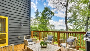 Une terrasse en bois, dotée de mobilier d’extérieur, d’un barbecue et offrant une vue sur les arbres et les collines.