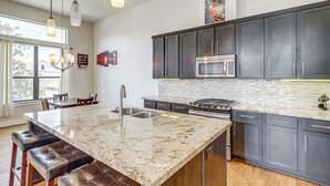 Une cuisine moderne avec des meubles de couleur sombre, un grand îlot central doté de sièges, des appareils électroménagers en acier inoxydable et une vue sur l’extérieur.