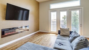 Un salon moderne doté d’un téléviseur à écran plat fixé au mur, d’une cheminée intégrée, d’un canapé gris et d’une grande porte-fenêtre coulissante donnant sur un balcon extérieur.