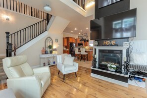 A spacious living room with a fireplace, a dining area, and a kitchen in the background. - Heated Pool, Hot Tub & Fire Pit in Ruby Park (Eugene)