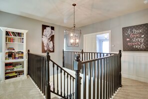 Una escalera con barandilla negra, un candelabro y una estantería llena de juegos.