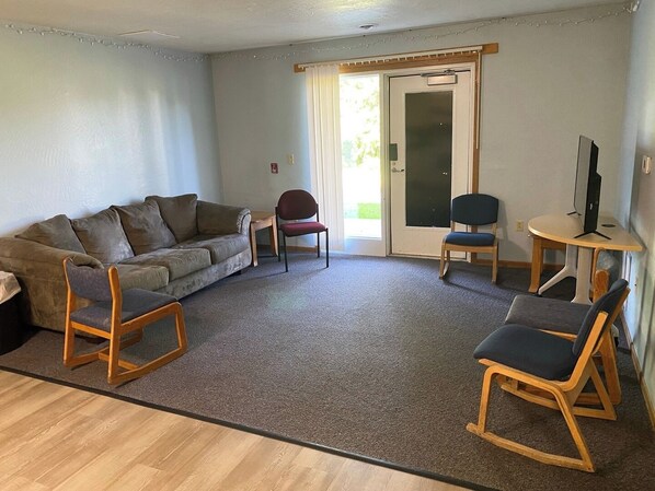 Ein Wohnzimmer mit einer Couch, zwei Schaukelstühlen, einem Tisch mit Fernseher und einer Tür, die nach draußen führt.