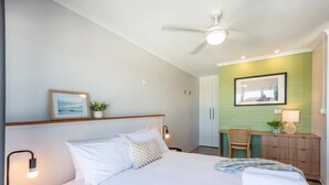 Une chambre d’hôtel avec un lit, un bureau, une chaise, un ventilateur de plafond et un mur vert.