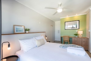 Een hotelkamer met een bed, een bureau, een stoel, een plafondventilator en een groene wand.