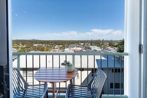 A balcony with a table and chairs, a potted plant, and a view of a town with buildings and trees.