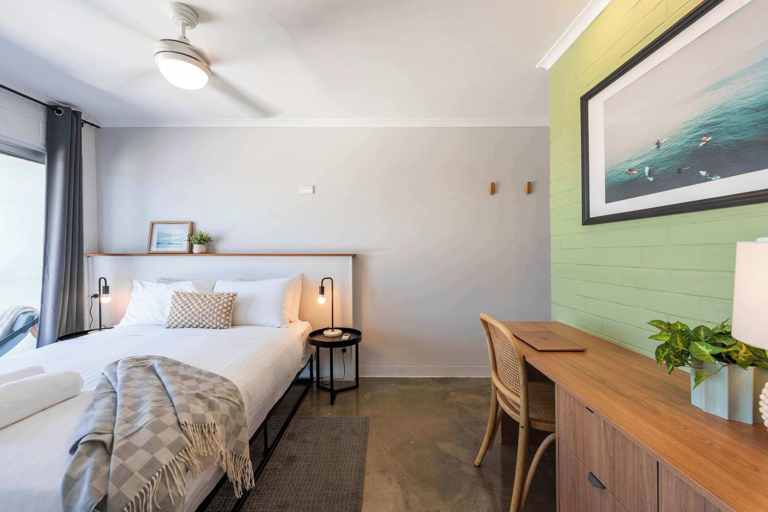 A hotel room with a bed, bedside table, lamp, chair, desk, and a large framed picture on the wall.