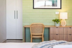 Um quarto com uma cama, uma escrivaninha com cadeira, uma luminária, uma planta e um quadro na parede.