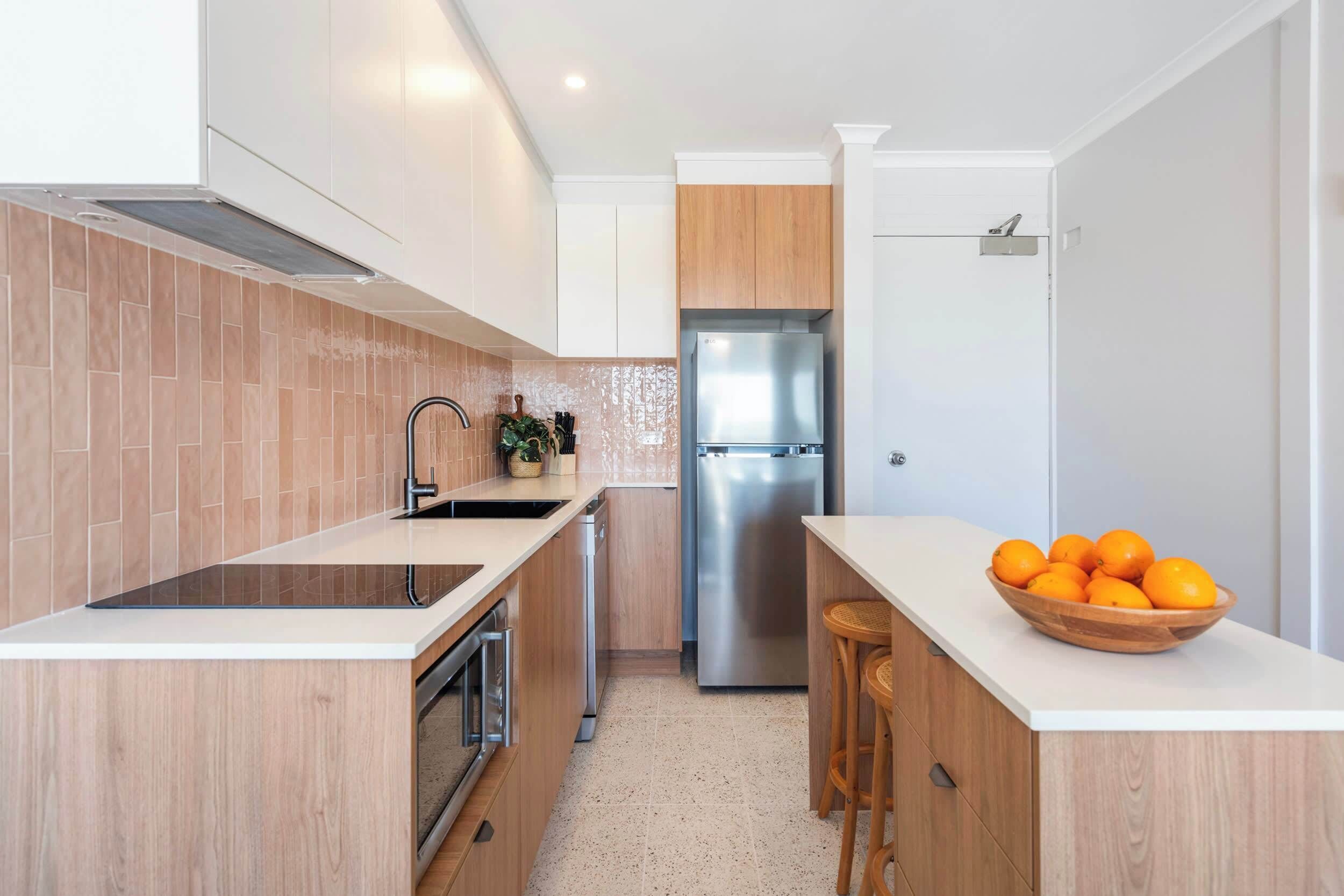 A modern kitchen with a stainless steel refrigerator, wooden cabinets, and a white countertop.