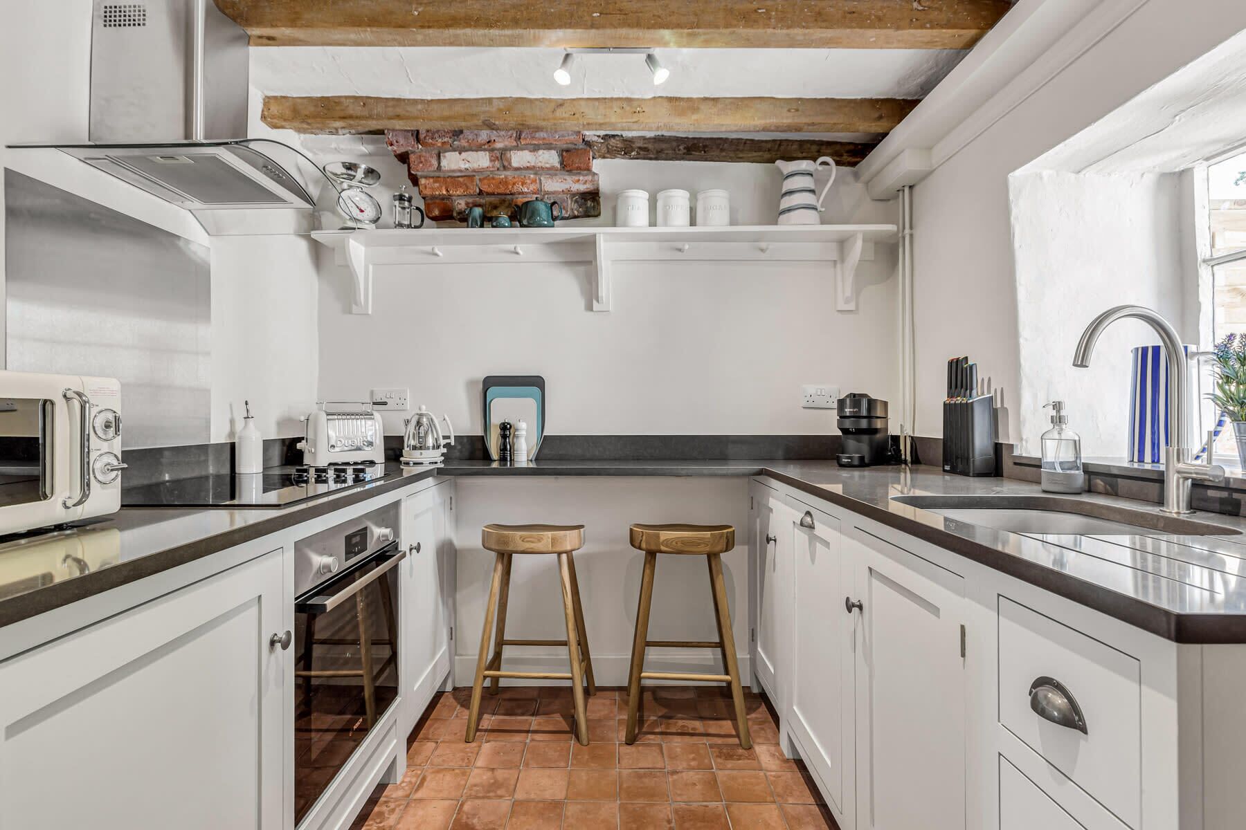 A kitchen with white cabinets, a brick wall, a microwave, a coffee maker, and two stools.