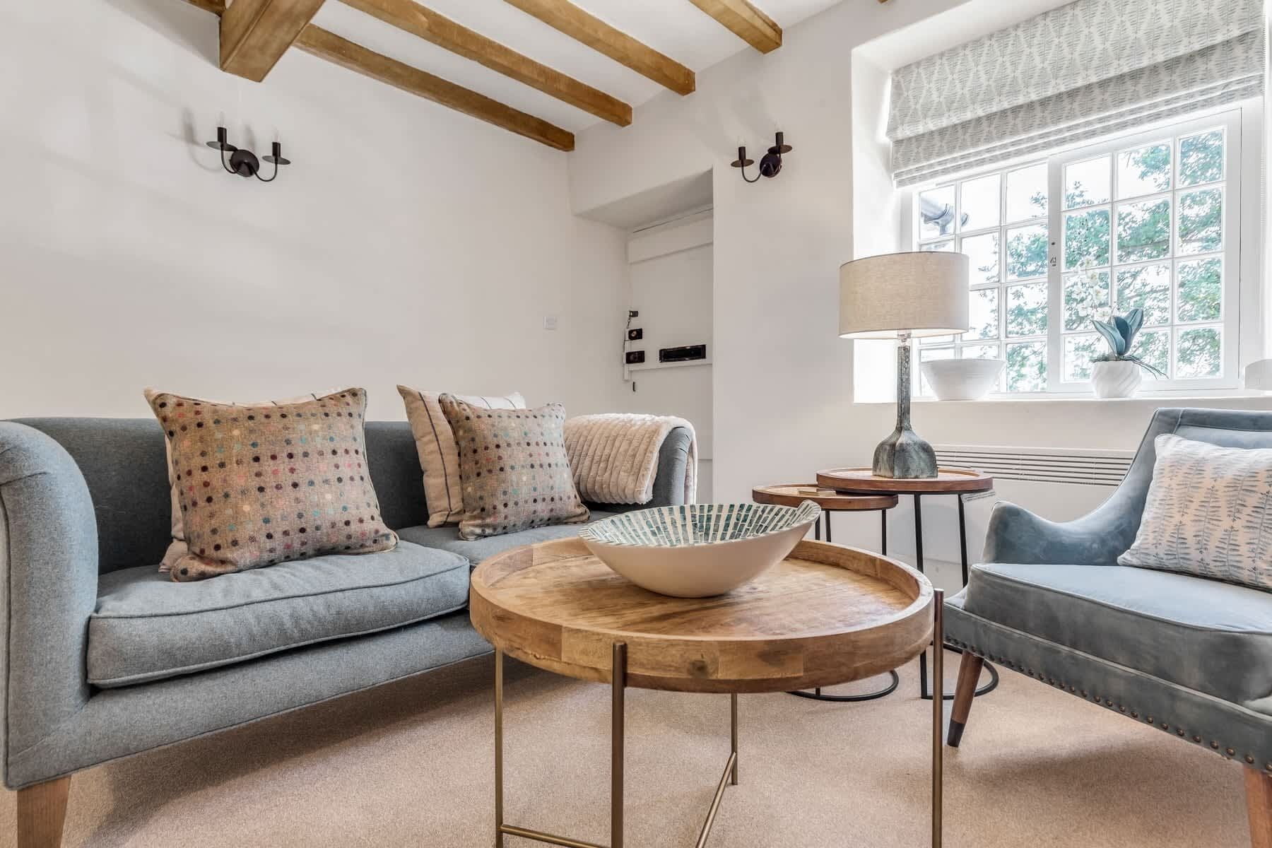 Ein modernes Wohnzimmer mit einem grauen Sofa, gemusterten Kissen, einem Holztisch und einer Lampe.