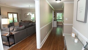 A spacious living room with a grey sofa, wooden flooring, and a dining area in the background.