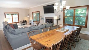 A spacious living room with a large wooden dining table, grey sectional sofa, and a fireplace.
