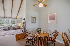 A dining area with a wooden table, four chairs, a ceiling fan, and a large window.