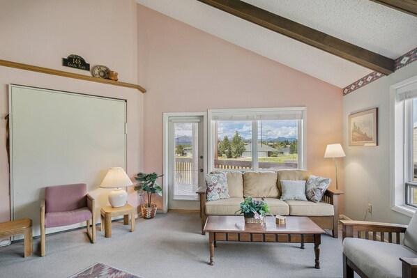 A living room with a sofa, armchairs, a coffee table, and a view of a residential area through large windows.