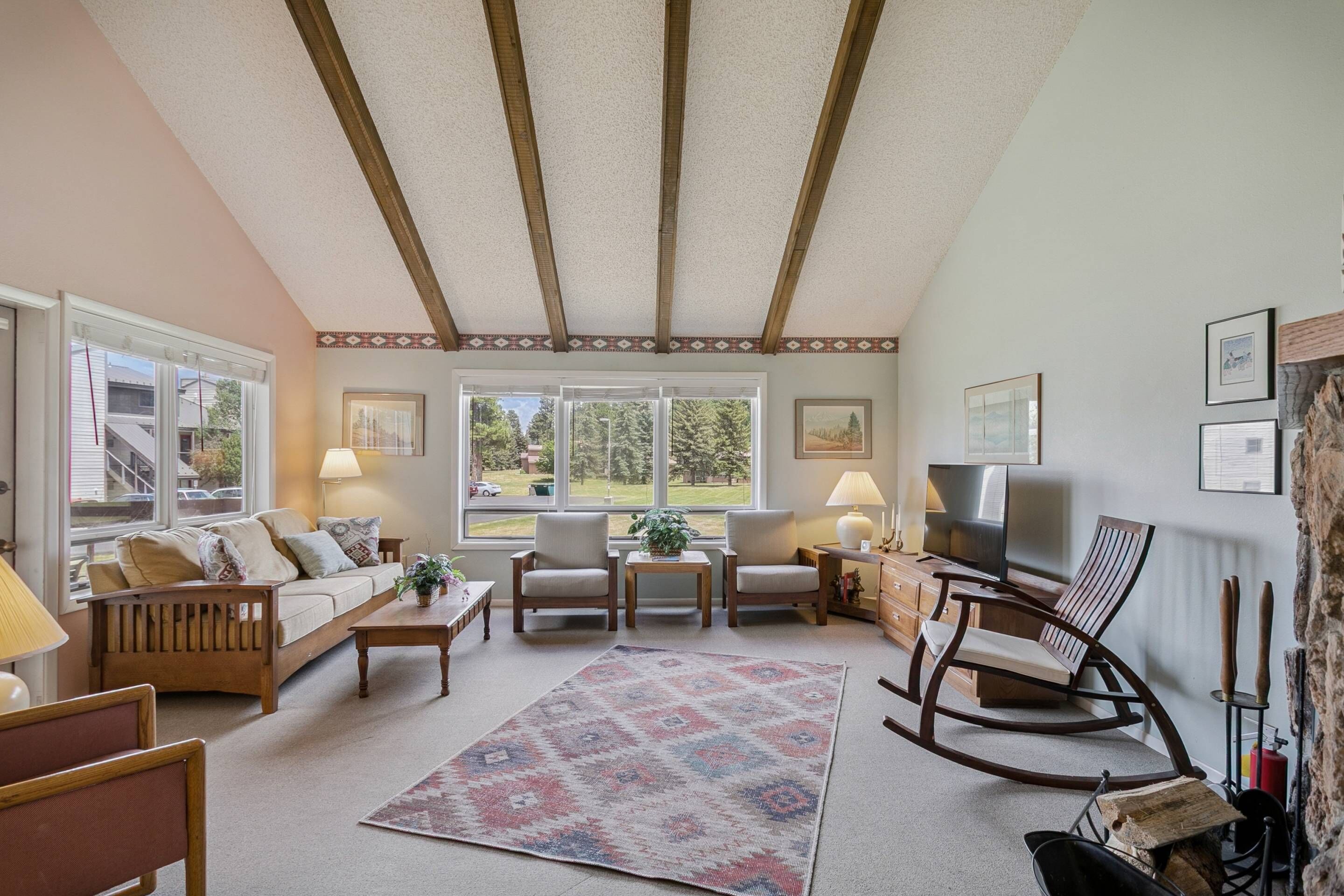 A cozy living room with a sofa, chairs, a TV, a fireplace, and a large window.