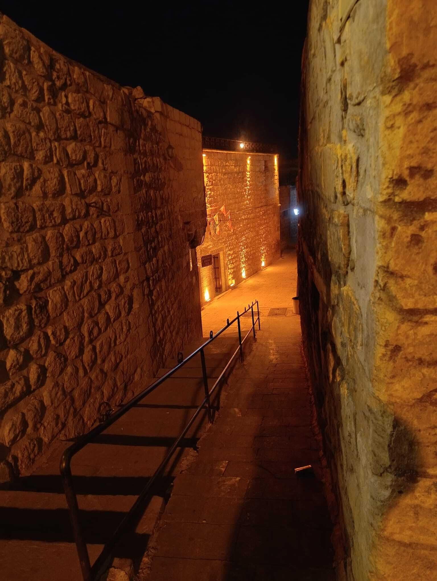 A narrow alleyway with stone walls and a metal railing.