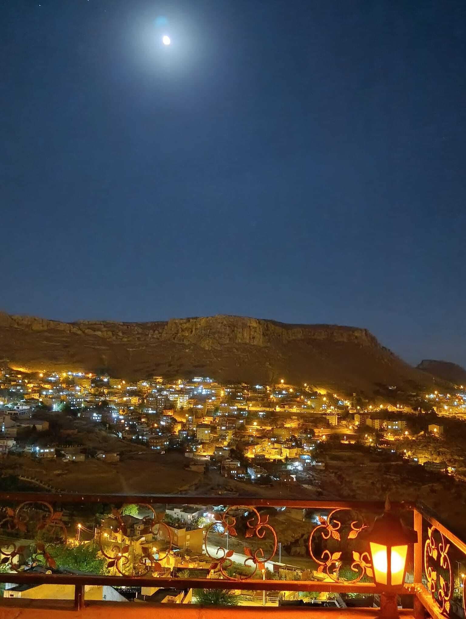Vista nocturna de un pueblo con una colina destacada al fondo y una barandilla de balcón con detalles decorativos.