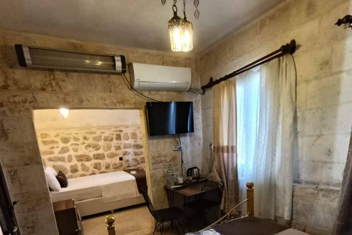 A bedroom with a stone wall, a bed, a desk, a TV, and a hanging light fixture.