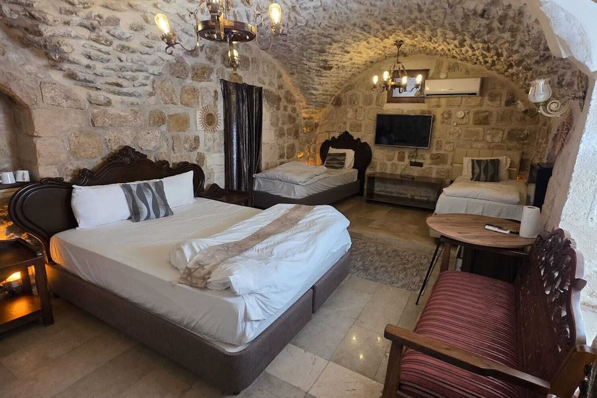 A stone-walled bedroom with a large bed, a smaller bed, a desk, and a chair.
