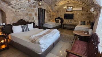 A stone-walled bedroom with a large bed, a smaller bed, a desk, and a chair.