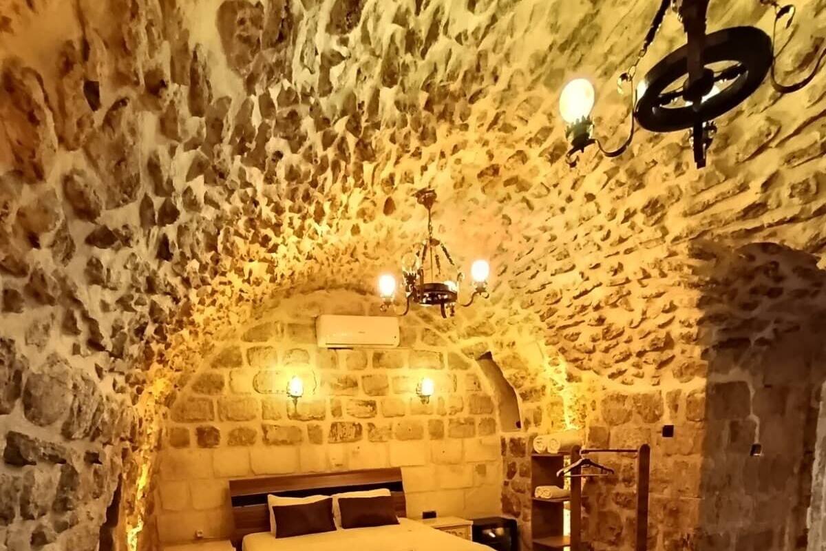 A cozy stone-walled room with a bed, a table with chairs, and a small kitchen area.