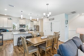 Una cocina moderna con armarios blancos, una isla central y una zona de comedor con mobiliario de madera.