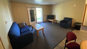 Ein Wohnzimmer mit einem blauen Sofa, einem roten Sessel, einem kleinen Tisch, einem Fernseher und einer Glaswand.