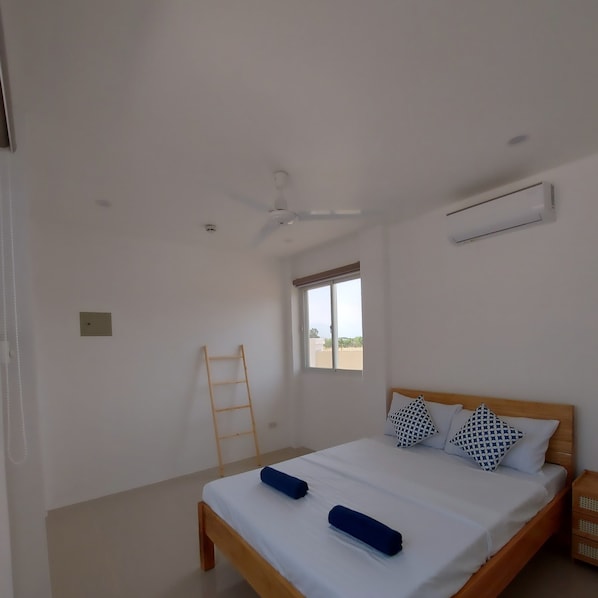 A bedroom with a bed, a ceiling fan, an air conditioning unit, a window, and a wooden ladder. - The Kubo Gardens (San Juan)