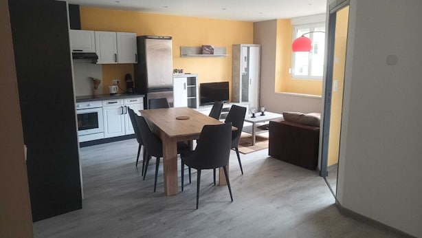 Eine moderne Küche mit weißen Schränken, einem Edelstahlkühlschrank und einem Essbereich mit einem Holztisch und schwarzen Stühlen.
