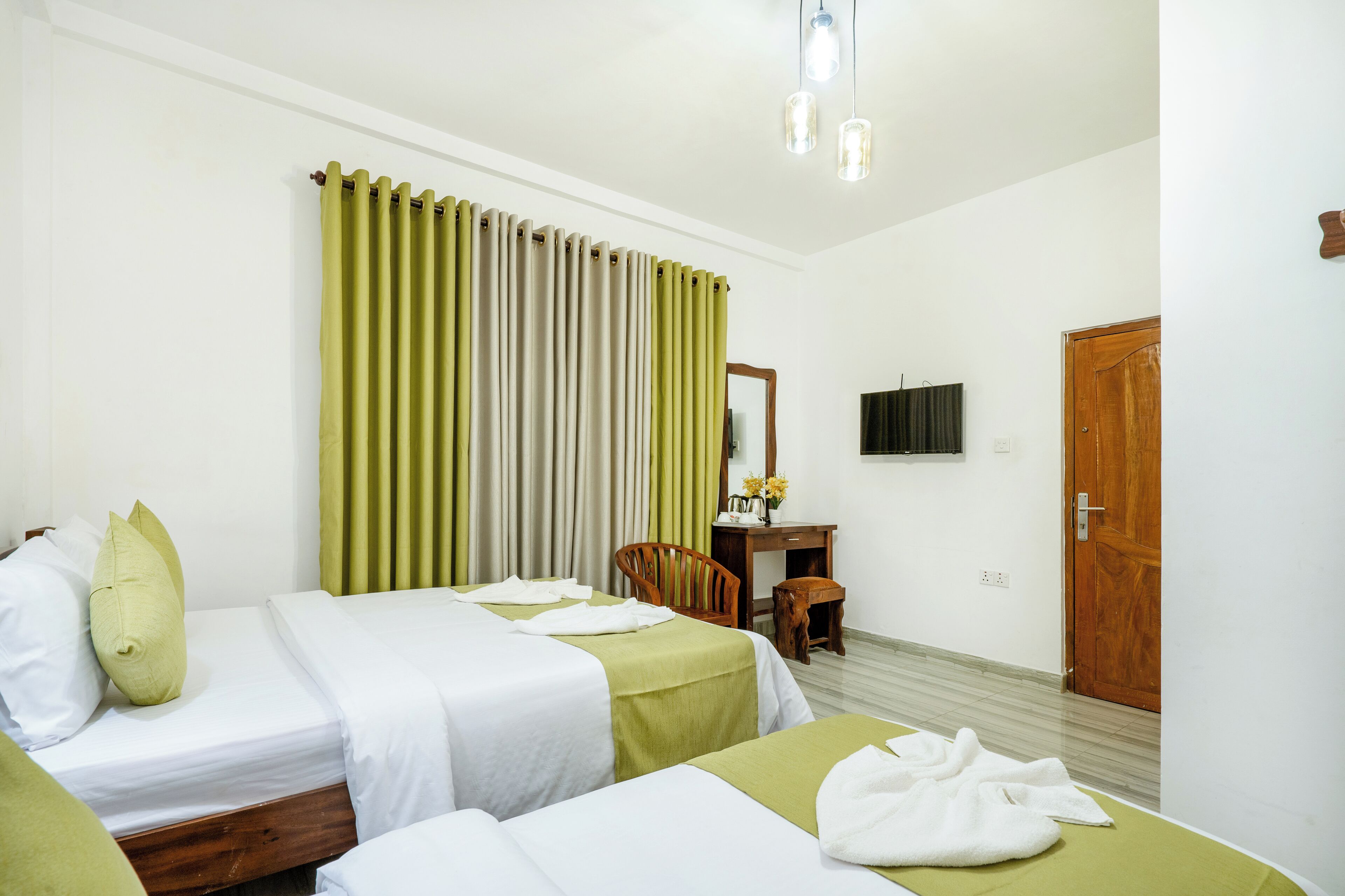 Habitación de hotel con dos camas, un escritorio de madera con espejo, una silla y un televisor en la pared.