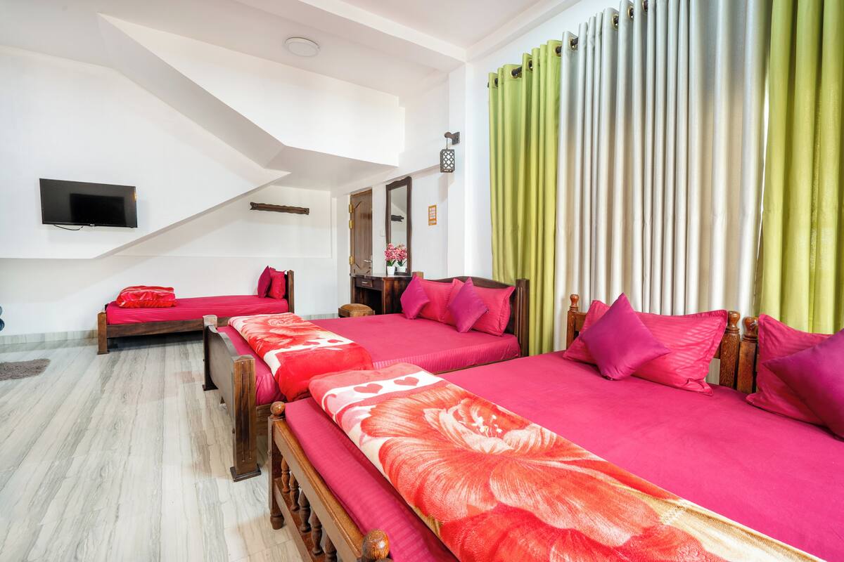 A hotel room with two beds, a flat-screen TV, a mirror, and a window with green curtains.