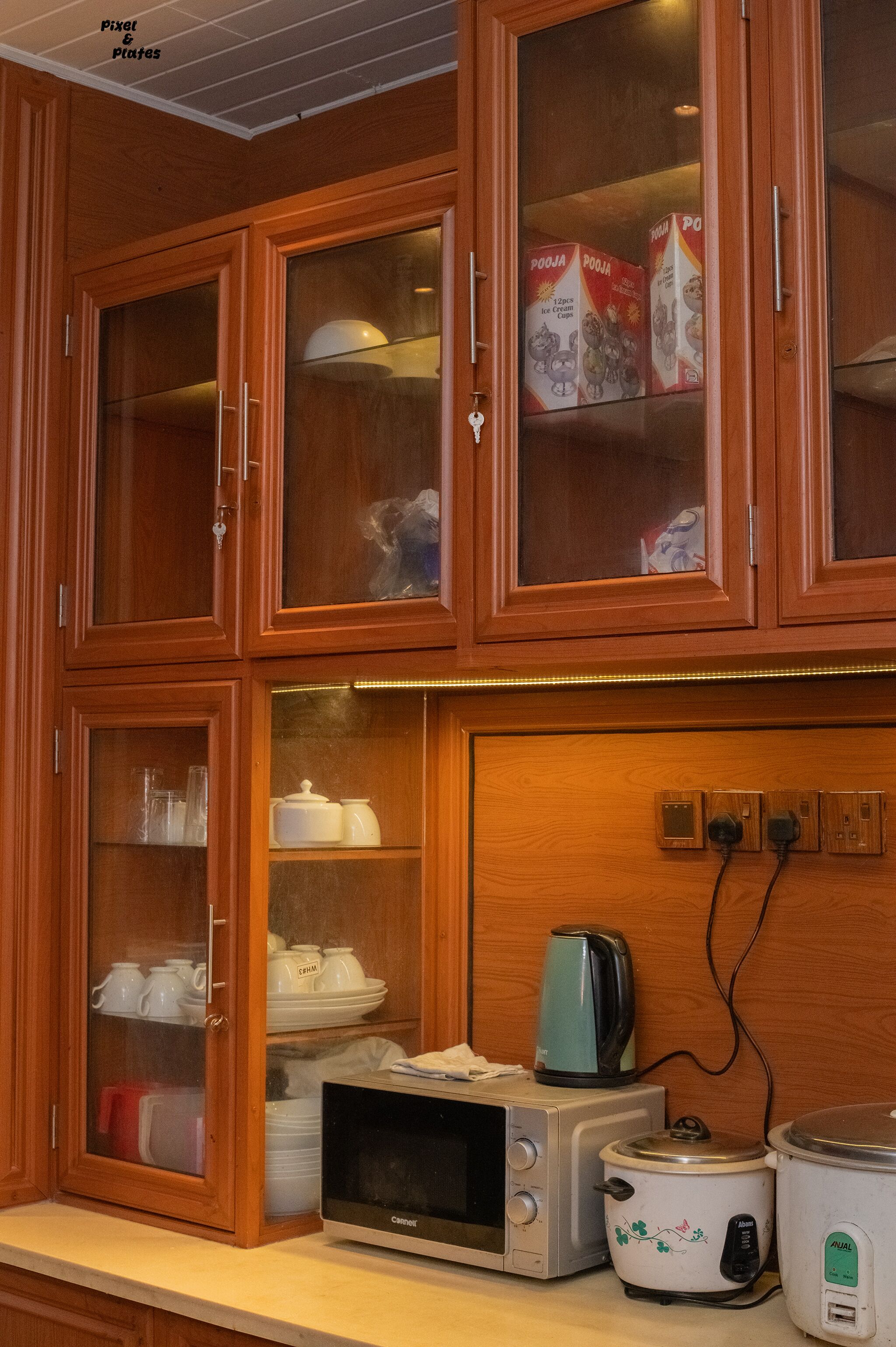 A kitchen with wooden cabinets, a microwave, a rice cooker, and a kettle.
